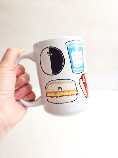 White mug featuring art of NYC foods held by a hand on a white background